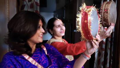 Two women in saris looking at the moon through decorated sieves on Karwa Chauth
