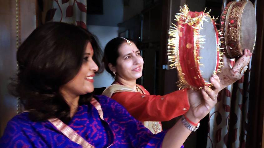 Two women in saris looking at the moon through decorated sieves on Karwa Chauth